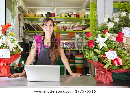 Portrait of a friendly and welcoming florist business woman owner proudly standing at the counter of a flower store using a laptop computer, smiling. Small business technology.
