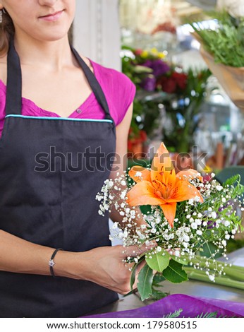 Faceless middle section hands detail view of a florist business woman owner at a flower shop market working and making a new floral arrangement. Small business owner.