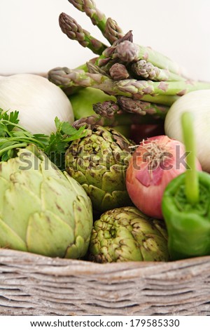 Close up view of a groceries basket full of various healthy and organic vegetables like artichockes, peppers, asparagus, onions and herbs in a home kitchen. Vegetarian food ingredients, interior.