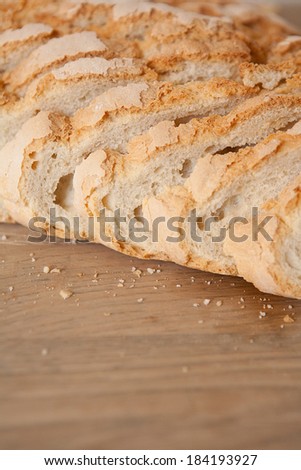 Macro close up detail of a home baked loaf of white bread with crunchy crust resting on a wooden kitchen table, cut in slices with a golden color. Food object in home interior.