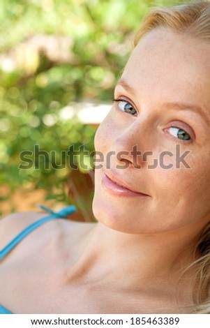 Close up beauty side portrait of an attractive blond Scandianvian woman relaxing on holiday in a green garden during a sunny summer day, smiling. Health and beauty lifestyle.