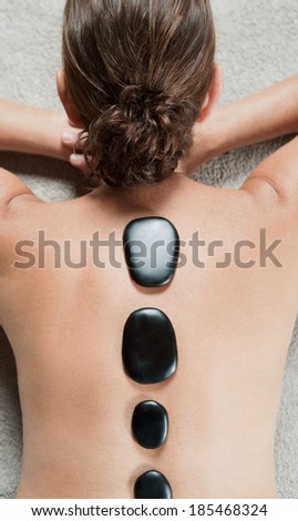 Over head rear view of an elegant mature woman\'s back relaxing and laying down in a health spa having a volcanic black stones heat treatment on her back. Beauty and health lifestyle.