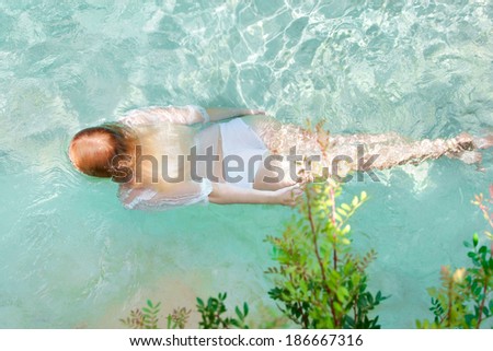 Over head view of a young woman swimming in the transparent blue waters of a health spa natural swimming pool, relaxing on a summer holiday, enjoying a swim during a sunny day, outdoors lifestyle.