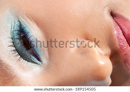 Over head beauty close up portrait of an attractive joyful young black woman eye and half face wearing colorful fantasy make up cosmetics, smiling outdoors. Aspirational beauty and lifestyle.
