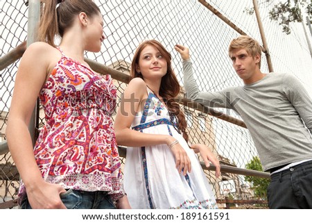 Close up portrait of a group of three diverse teenager friends relaxing together on a college campus sports ground looking cool and smiling during a break. Students outdoors lifestyle.