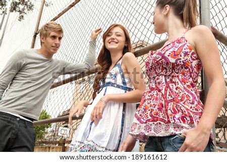 Close up portrait of a group of three diverse teenager friends relaxing together on a college campus sports ground looking cool and laughing during a break at university. Students outdoors lifestyle.