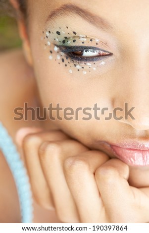 Detail close up portrait of an african american young black woman leaning her chin on her hand, wearing spotty eye shadow make up cosmetics and glossy lips, with a chic expression. Beauty lifestyle.