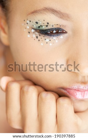 Detail close up portrait of an african american young black woman leaning her chin on her hand while wearing spotty eye shadow make up cosmetics and glossy lips, thoughtful. Beauty lifestyle.