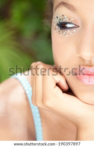Close up portrait of an attractive african american young black woman leaning her chin on her hand, wearing spotty eye shadow make up and glossy lips, with a surprise expression. Beauty lifestyle.