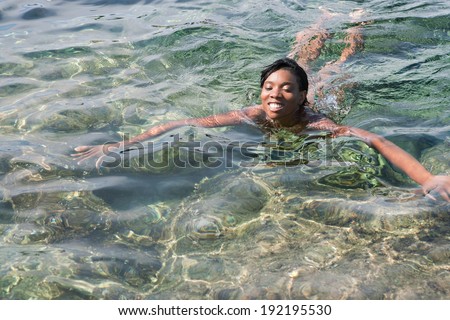 Beautiful young african american black woman swimming naked in a clear transparent blue sea during a sunny summer day on holiday. Travel and healthy lifestyle, outdoors.