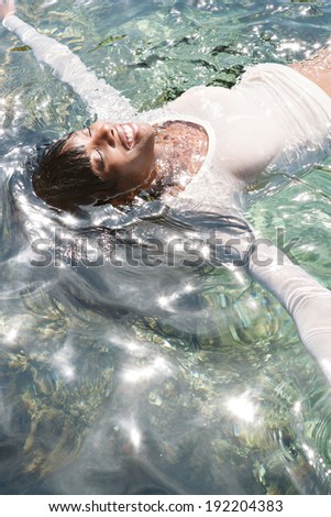 Over head portrait view of a beautiful african american woman floating in the sun shining and glittering blue sea water, smiling with her arms outstretched, relaxing on holiday. Travel lifestyle.