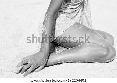Black and white close up of a beautiful young african american black woman lower legs section relaxing sunbathing on a beach with sand grains on her dark skin on vacation. Travel holiday lifestyle.