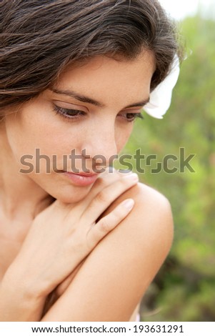 Beauty portrait of a young serene woman with perfect skin relaxing in nature with bare shoulders and wearing a white flower in her hair during a summer holiday, outdoors. Health and beauty lifestyle.