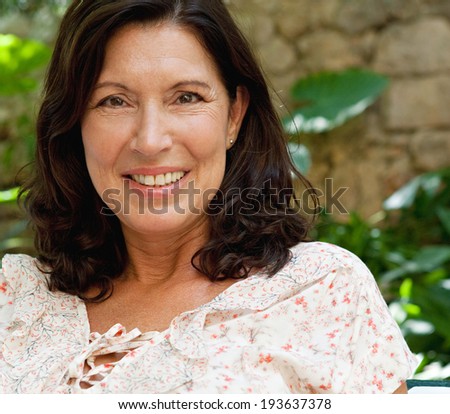 Close up portrait of a beautiful and fresh senior woman sitting in a luxury hotel garden on holiday smiling and relaxing on vacation. Mature healthy people outdoors. Senior people lifestyle.