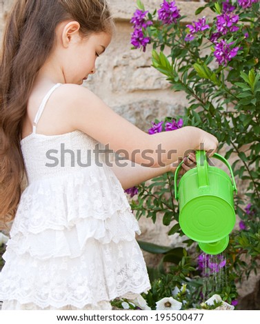 Side portrait of a beautiful young child girl holding a watering can and watering the plants in her holiday home garden, focused outdoors. Kid helping with home duties while on vacation, lifestyle.