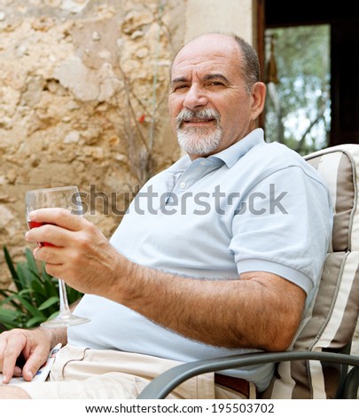 Portrait of a mature man in a luxury home garden on holiday drinking rose wine and relaxing on a summer vacation. Senior people enjoying travel and retirement drinking alcohol outdoors, lifestyle.