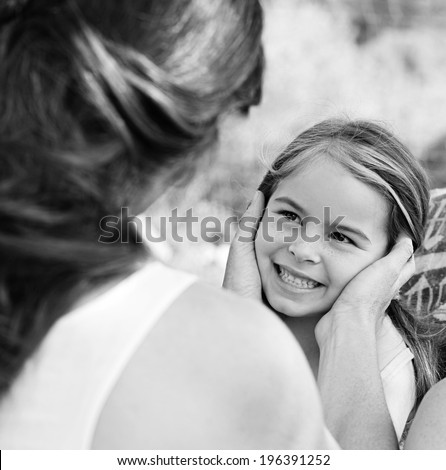 Rear view of a young mother holding her young daughter face in her hands while sitting together in a holiday home garden during a summer vacation. Family activities and lifestyle outdoors.
