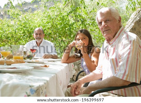 Portrait of a joyful family gathering around a healthy lunch food eating table outdoors during a summer holiday in a vacation garden home. Fun eating and family enjoying the sun, lifestyle.