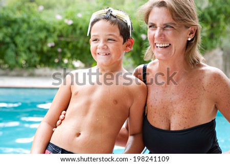 Close up portrait of a joyful mother and son enjoying a summer day together in a holiday home garden and swimming pool, laughing and being active. Vacation and relaxing family lifestyle, outdoors.