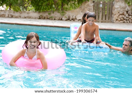 Father and children enjoying a summer holiday in a hotel swimming pool, playing games and floating in lilos during a summer vacation together. Active family lifestyle, outdoors.