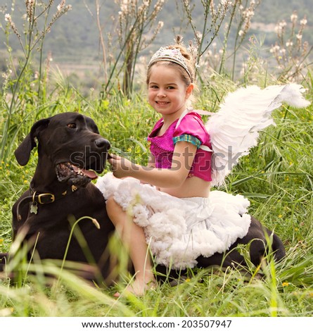 Side view of a pretty girl wearing a pink fancy dress with wings, sitting on her dogs back enjoying a sunny holiday in a green park field, smiling outdoors. Active family with animal pets, lifestyle.