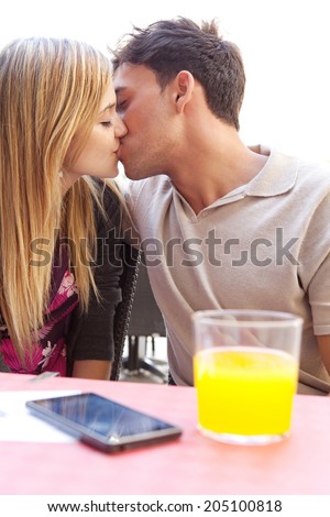 Side portrait of attractive young couple on holiday being romantic and holding their foreheads together while sitting at a coffee terrace bar drinking refreshments during a summer vacation, outdoors.