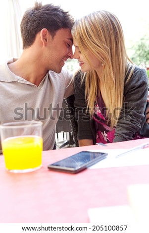 Profile portrait of attractive young couple on holiday being romantic and kissing while sitting at a coffee terrace bar drinking refreshments during a summer vacation. Love and relationships outdoors.