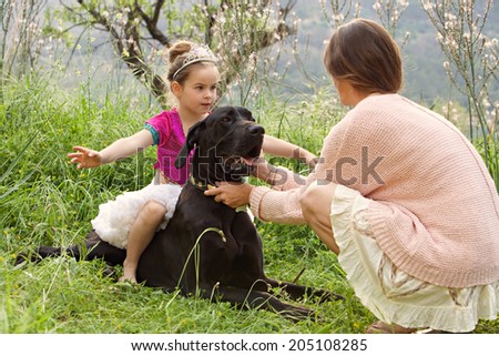 Mother and young daughter relaxing together with their pet dog in a lush green field on holiday during a sunny day. Animal pets, friendship and companionship. Active family playing with their dog.