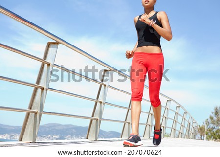 Wide view of an athletic young african american woman running and exercising by the seaside during a sunny day. Health and fitness body care and training outdoors.