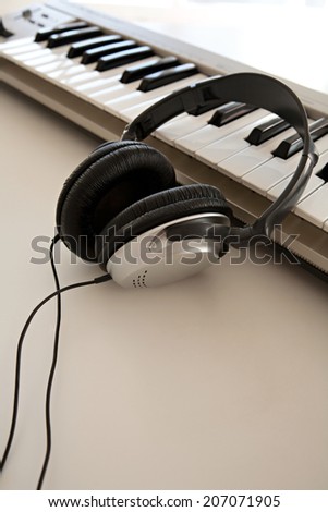 Still life of two electronic music and sound devices laying together on a white desk in a recording studio, interior. Detail view of a pair of headphones and a keyboard, technology.