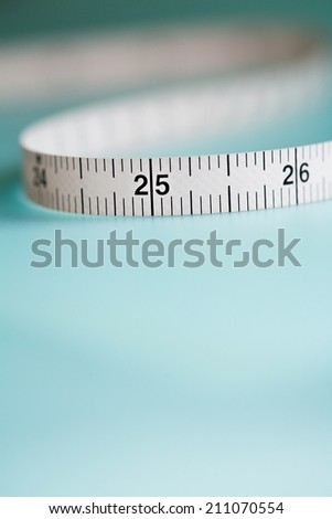 Close up still life detail view of a soft tailor measuring tape laying in a curly shape on a plain blue background, interior. Trade tools and objects for exact measure taking.