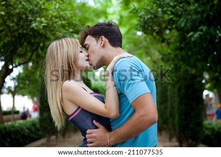 Side portrait view of a passionate romantic young couple kissing and embracing while in a green park on holiday. Young people romantic lifestyle and love, outdoors.