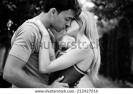 Side black and white portrait of a passionate romantic young couple kissing and embracing while in a park on holiday. Young people romantic lifestyle and love, outdoors.