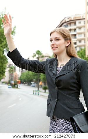 Attractive professional young business woman standing in a financial city street calling a taxi and holding up her arm. Business people commuting and using public transport to get to work.