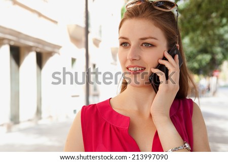 Close up portrait of a beautiful young business woman using a smartphone in the city to make a call and have a conversation, smiling in a classic street. Professional woman using technology outdoors.