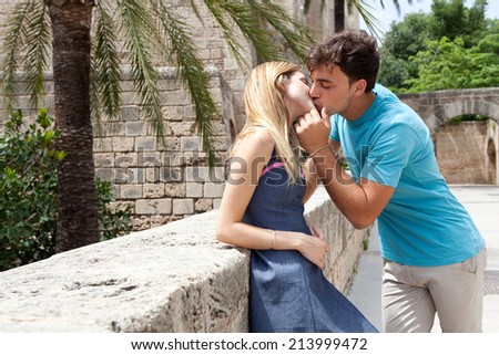 Young attractive tourist couple being close and in love, kissing and hugging with passion and romance while on holiday, visiting a touristic destination city monumental architecture, outdoors.