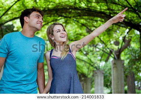 Portrait of a young tourist couple visiting a green garden park on a weekend city travel break, pointing at monumental sights. Loving girlfriend and boyfriend enjoying a summer holiday outdoors.