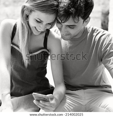 Black and white portrait of a young tourist couple using a smartphone to network while on holiday, visiting a touristic destination city and having fun outdoors. Sharing technology outdoors.