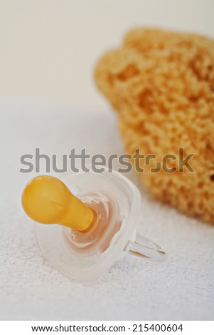 Still life close up view of a new born baby dummy laying next to a towel and a natural sponge ready for a baby bath, on a plain white background indoors. Detail of baby care items.