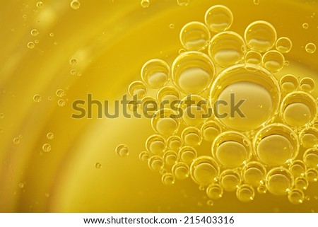 Over head close up full frame background detail view of abstract golden shining yellow oil boiling and creating bubbles, indoors. Macro still life view of oil bubbles texture and detail.