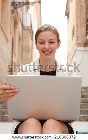 Portrait of an attractive young professional business woman sitting on the steps of an old stone building street using a laptop computer working outdoors. Connectivity and wireless internet browsing.