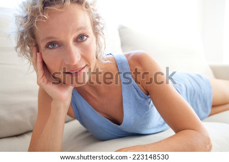 Beauty portrait of an attractive middle aged healthy woman relaxing on a white sofa at home, laying down relaxing and smiling. Interior home living and well being lifestyle.