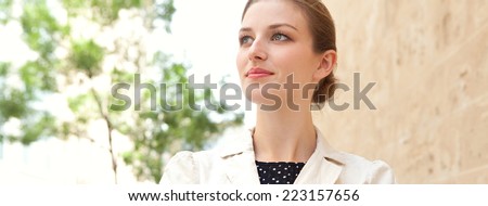 Spacious panoramic portrait of an attractive young executive business woman wearing stylish professional clothing in a city street, thoughtful outdoors. Business people and aspirational lifestyle.