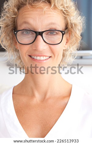 Close up portrait of a joyful professional successful woman smiling at the camera feeling confident in an office interior. Business woman with reading glasses and a cheerful face expression, indoors.