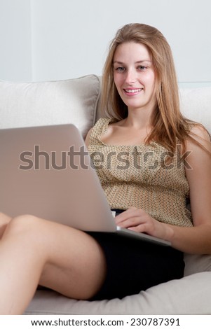 Attractive professional business woman using a laptop computer to browse the internet on line, sitting on a spacious white wall living room with a comfortable white sofa, home interior.