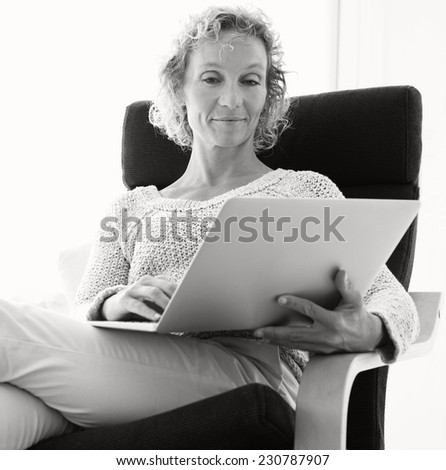 Black and white portrait of healthy successful professional woman relaxing at home using a laptop computer for internet on line recreational leisure, interior. Technology and lifestyle at home.
