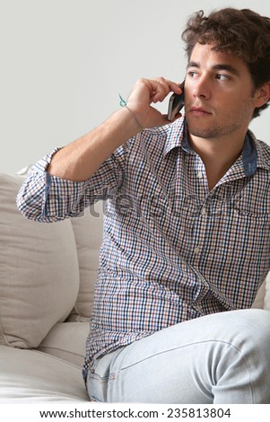 Working business man having a phone conversation on a smart phone working from home office. Young professional man using technology in a home living room, interior.