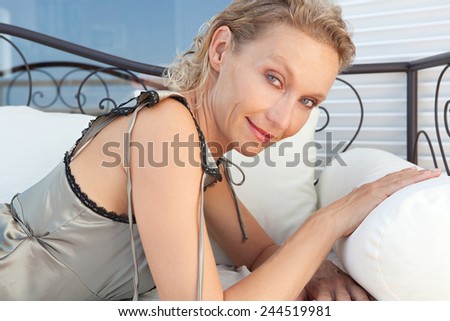 Close up beauty portrait of a mature healthy and attractive woman laying down lounging and relaxing on a day bed in an exterior home. Wellness, well being and senior care lifestyle, smiling.