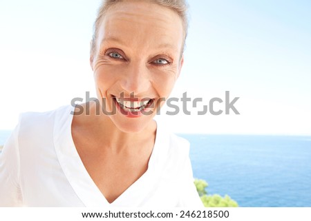 Close up beauty portrait of happy and joyful woman showing a fun and carefree expression of joy against a blue sky and sea background. Feelings and emotions in lifestyle. Gestures and expressions.