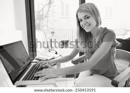 Black and white portrait of young professional woman smiling in her home office space, joyfully looking at the camera. Student girl using a laptop computer at home. Lifestyle and technology, interior.